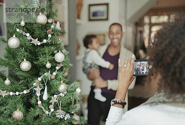 Frau fotografiert Mann und kleine Tochter am Weihnachtsbaum