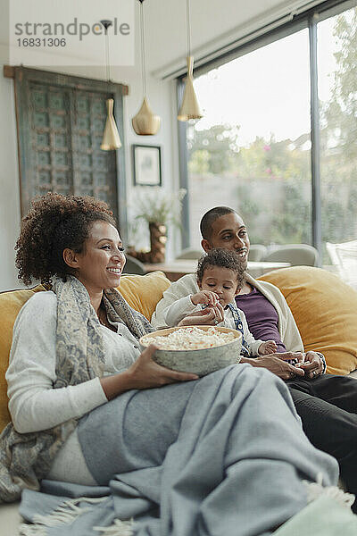 Familie schaut Film und isst Popcorn auf dem Wohnzimmersofa