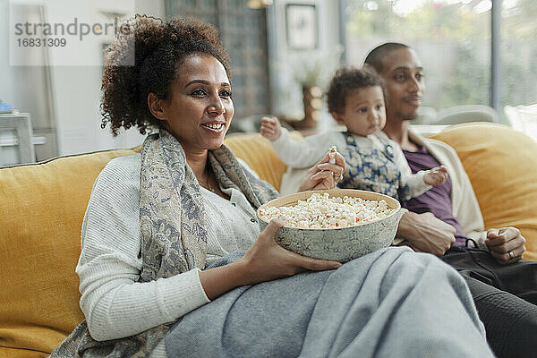 Glückliche Familie beobachten Film und essen Popcorn auf Sofa im Wohnzimmer