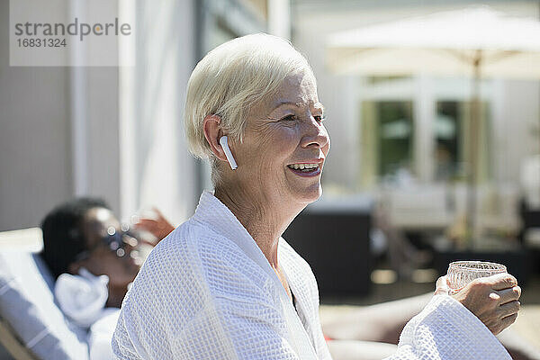 Glückliche ältere Frau mit Ohrstöpsel-Kopfhörer auf der sonnigen Hotelterrasse