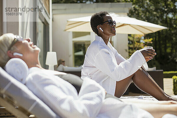 Sorglose ältere Frauen in Wellness-Bademänteln entspannen sich auf der sonnigen Hotelterrasse