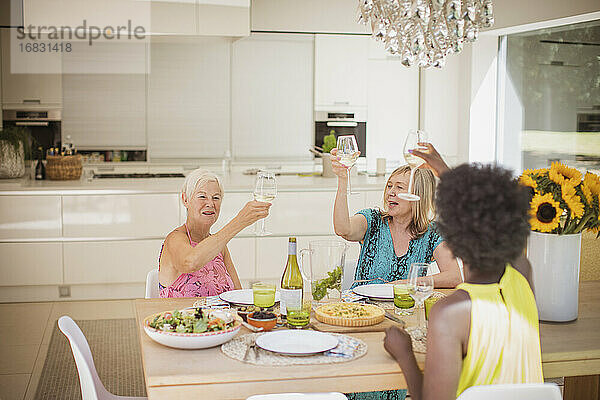Glückliche Seniorinnen stoßen beim Mittagessen mit Weingläsern an