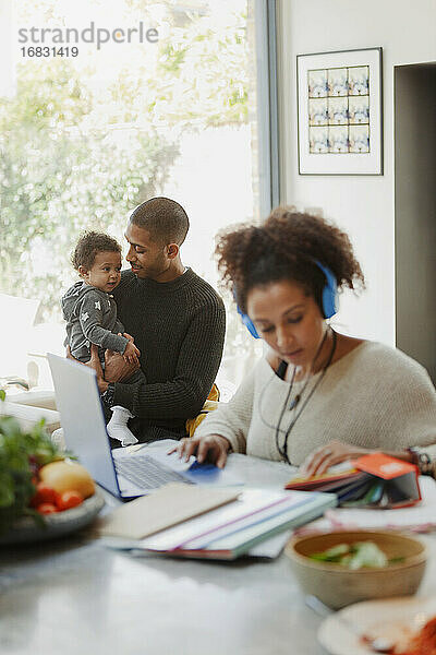 Vater hält Baby Tochter hinter arbeitenden Mutter am Laptop