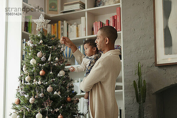 Vater und kleine Tochter schmücken Weihnachtsbaum im Wohnzimmer