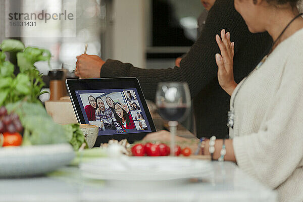 Familie beim Videochat auf dem digitalen Tablet-Bildschirm und bei der Zubereitung des Abendessens