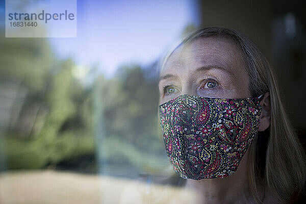 Besorgte Seniorin mit Gesichtsmaske am Fenster