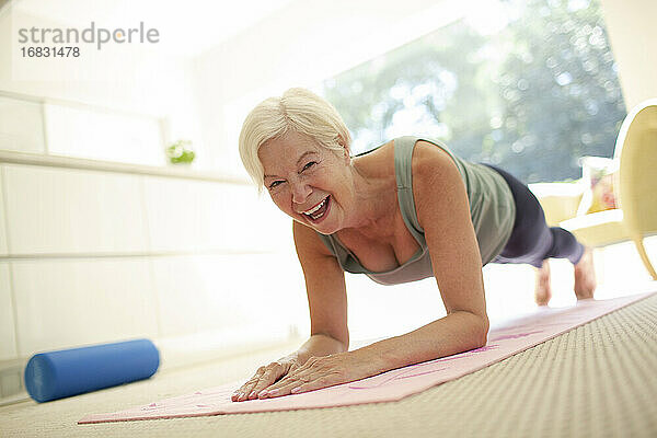 Porträt glücklich ältere Frau übt Planke Pose auf Yoga-Matte zu Hause