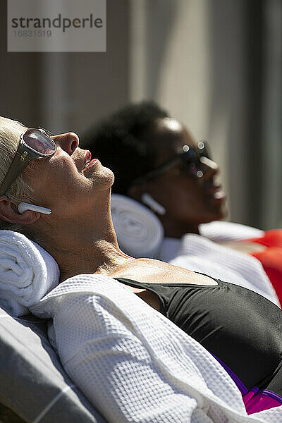 Seniorin mit Ohrstöpsel-Kopfhörer beim Sonnenbaden auf sonniger Terrasse