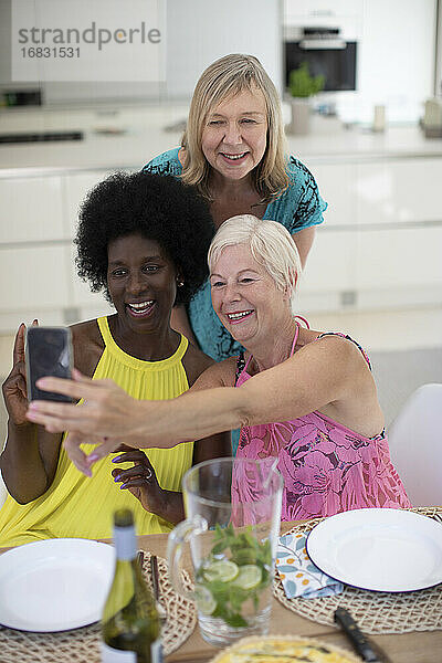 Glückliche ältere Frauen Freunde in Kleidern nehmen selfie am Esstisch