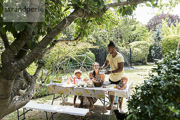 Vater serviert der Familie am sommerlichen Hinterhoftisch Barbecue