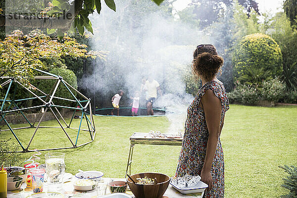 Frau grillen und beobachten Familie spielen auf Hinterhof Trampolin