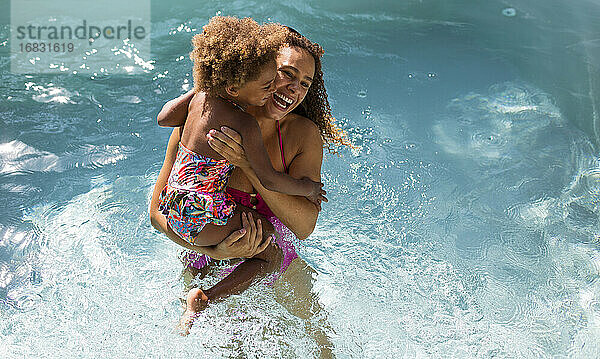 Glückliche Mutter hält Tochter im sonnigen Sommer Schwimmbad