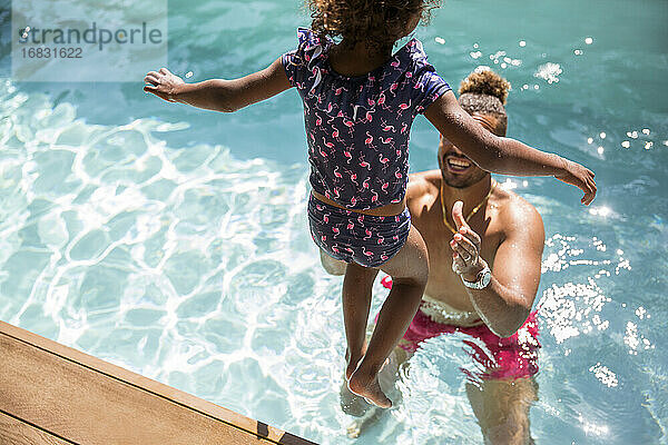 Tochter springt in die Arme des Vaters im sonnigen Schwimmbad