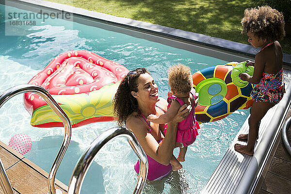 Mutter und Töchter spielen im sonnigen Sommer Schwimmbad