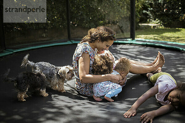 Mutter und Töchter spielen auf Hinterhof Trampolin mit Hunden