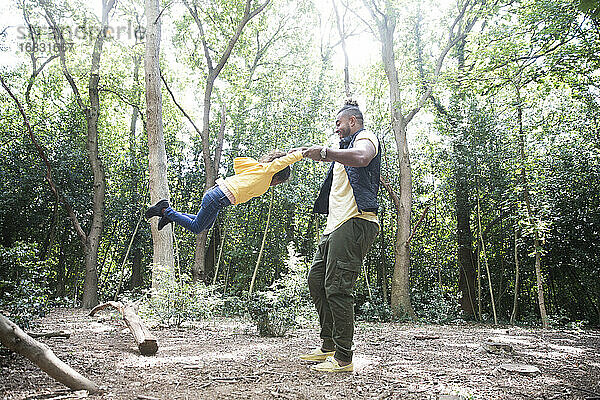 Playful Vater schwingt Tochter unter Bäumen in sonnigen Wald