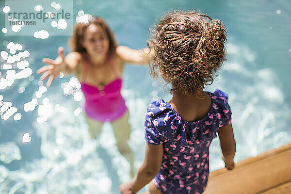 Tochter bereitet sich auf den Sprung in die Arme der Mutter im sonnigen Schwimmbad vor
