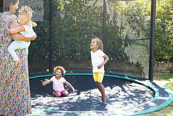 Glückliche Mutter und Töchter spielen auf sonnigen Hinterhof Trampolin