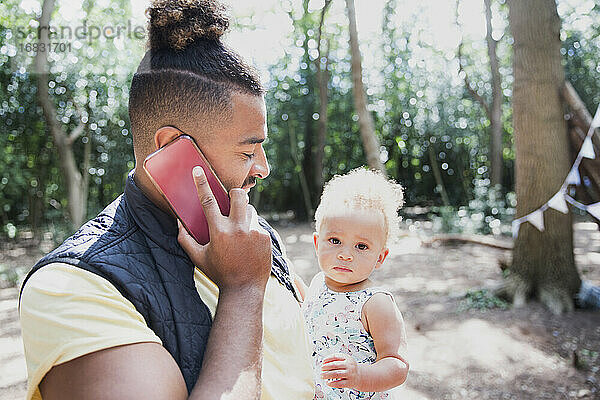 Vater hält Kleinkind Tochter und sprechen auf Smartphone im Wald