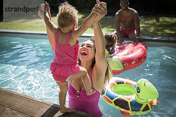 Playful Mutter Heben Kleinkind Tochter in sonnigen Schwimmbad