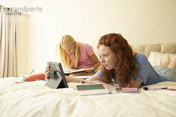 Preteen Mädchen Freunde mit digitalen Tablet machen Hausaufgaben auf dem Bett