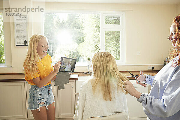 Glücklich preteen Mädchen mit digitalen Tablette Schneiden Mutter Haare in der Küche