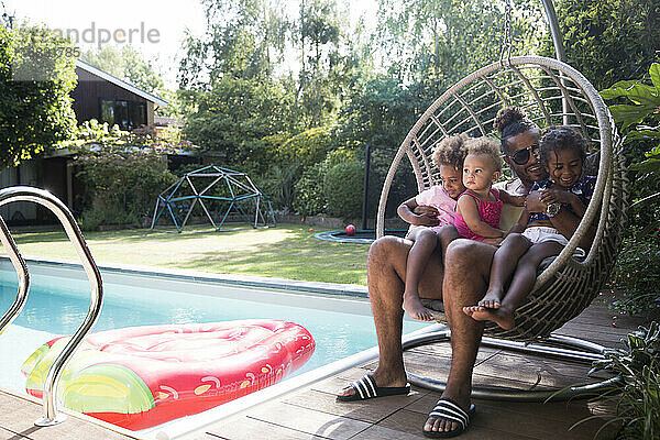 Glückliche Vater und Töchter kuscheln in Sommer Poolside Schaukel Stuhl