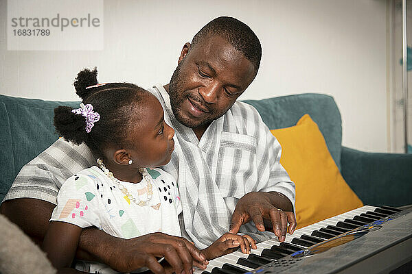 Zärtlicher Vater und Tochter spielen Keyboard-Klavier auf Sofa