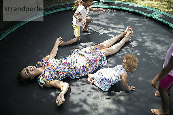 Töchter spielen um sorglose Mutter auf dem Trampolin liegend