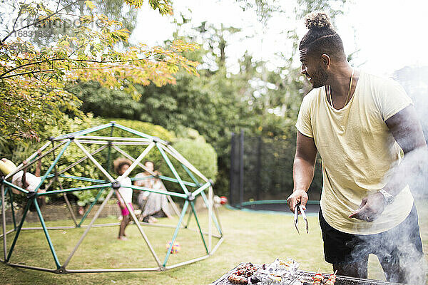 Vater grillen am Grill und beobachten Kinder spielen im Sommer Hinterhof