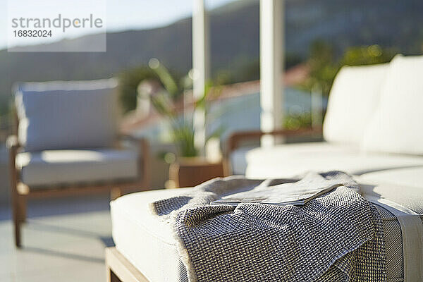 Decke und Zeitschrift auf sonnigem Terrassensofa