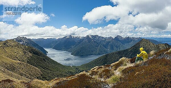 Bergsteiger  Wanderer sitzt im Gras  Blick auf den South Fiord des Lake Te Anau  hinten Murchison Mountains und Südalpen  am Wanderweg Kepler Track  Fiordland National Park  Southland  Neuseeland  Ozeanien