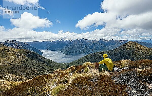 Bergsteiger  Wanderer sitzt im Gras  Blick auf den South Fiord des Lake Te Anau  hinten Murchison Mountains und Südalpen  am Wanderweg Kepler Track  Fiordland National Park  Southland  Neuseeland  Ozeanien