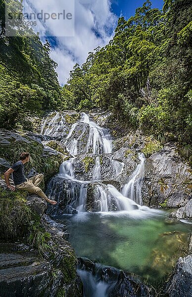 Junger Mann sitzt an einem Wasserfall  Fantail Falls  Makarora River  Wanaka  Westcoast  Südinsel  Neuseeland  Ozeanien