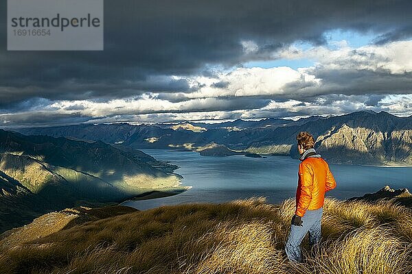 Wanderer blickt in die Ferne  Blick auf Lake Hawea im Abendlicht  See und Berglandschaft  Ausblick vom Isthmus Peak  Wanaka  Otago  Südinsel  Neuseeland  Ozeanien