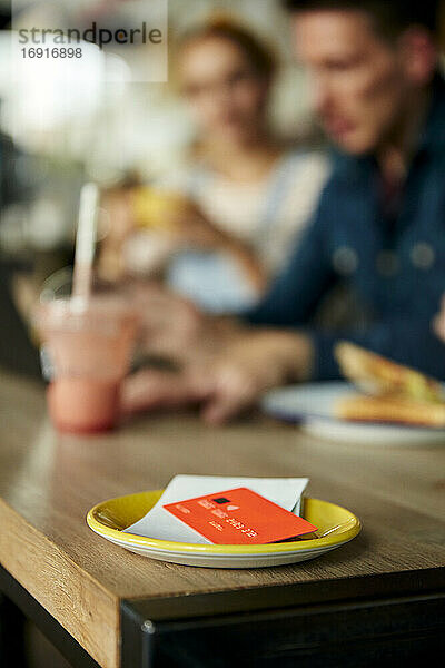 Menschen an einem Cafe-Tisch  eine Untertasse mit Kassenbon und Kreditkarte.