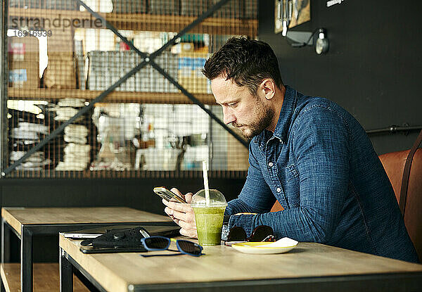 Mann sitzt allein am Tisch mit Laptop und Saft Getränk im Café mit Smartphone