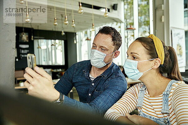 Zwei Personen mit Gesichtsmasken  die ein Smartphone benutzen  winken während eines Face-Time-Anrufs.