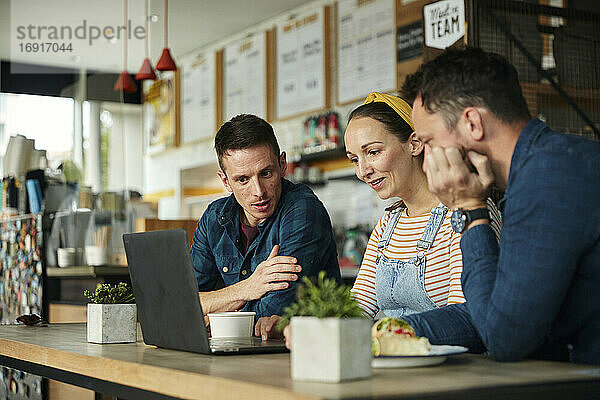 Zwei Männer und eine Frau  die in einem Café sitzen und auf einen Laptop schauen