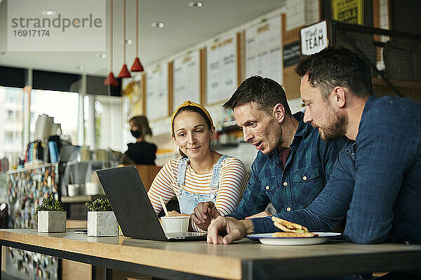 Zwei Männer und eine Frau  die in einem Café sitzen und auf einen Laptop schauen