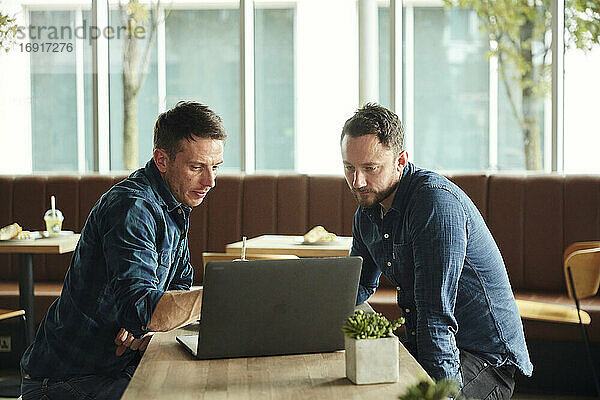 Zwei Männer  die in einem Café sitzen und auf einen Laptop-Bildschirm schauen