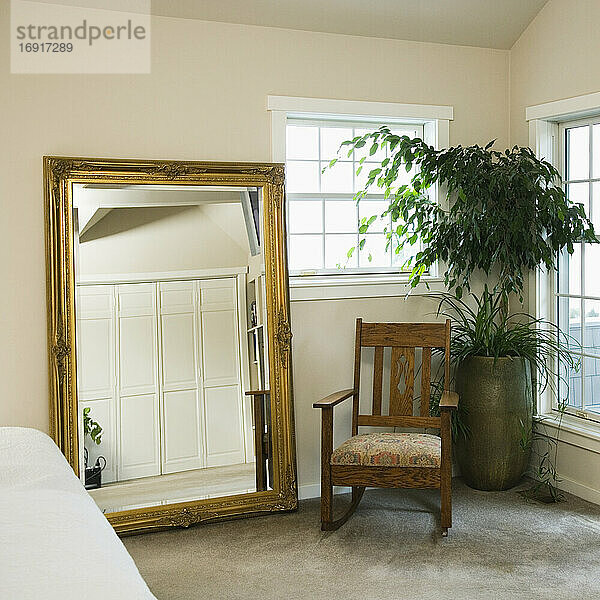 Goldspiegel und Schaukelstuhl mit Topfpflanze im Schlafzimmer.