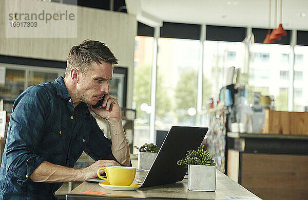 Mann in einem Café sitzend  an einem Laptop arbeitend