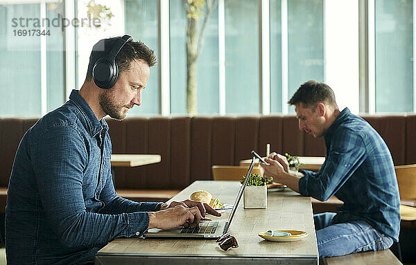 Zwei Männer sitzen in einem Café und arbeiten aus der Ferne mit einem Laptop und einem Smartphone