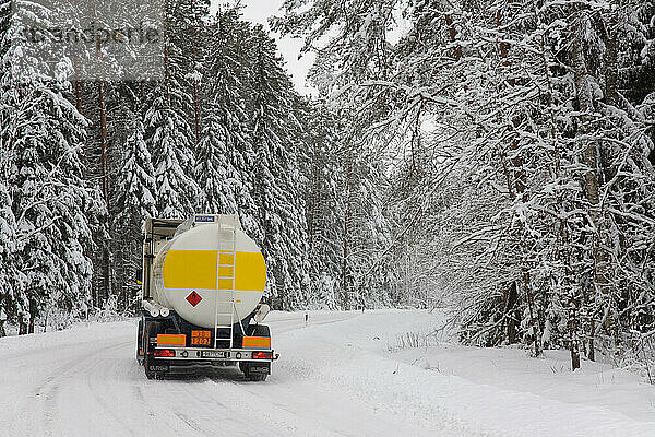 Lastwagenfahrt auf verschneiter Landstraße durch Wald.