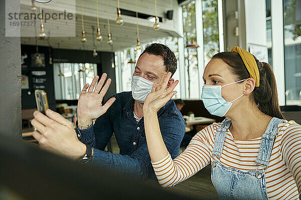 Zwei Personen mit Gesichtsmasken  die ein Smartphone benutzen  winken während eines Face-Time-Anrufs.