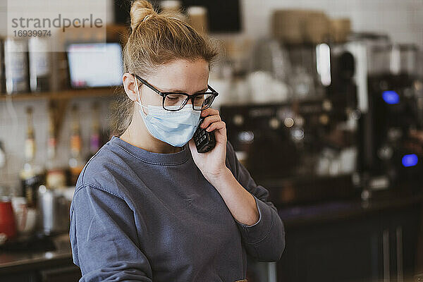 Kellnerin mit Gesichtsmaske bei der Arbeit in einem Café  am Telefon.