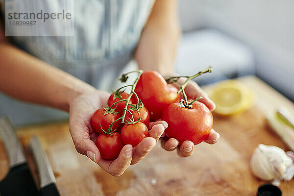 Frau hält unterschiedlich große Bio-Tomaten in der Küche