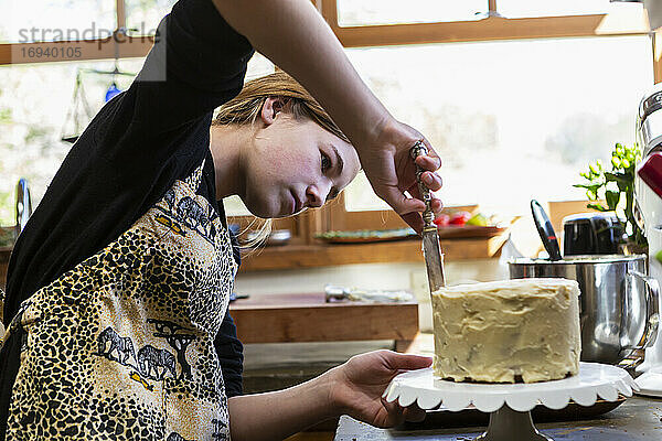 Teenager-Mädchen in der Küche Anwendung Zuckerguss auf Kuchen