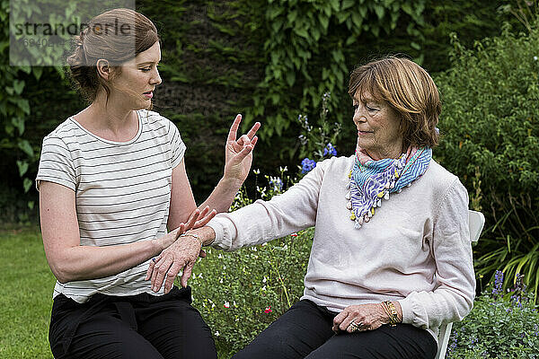 Frau und Therapeutin bei einer alternativen Therapiesitzung in einem Garten.